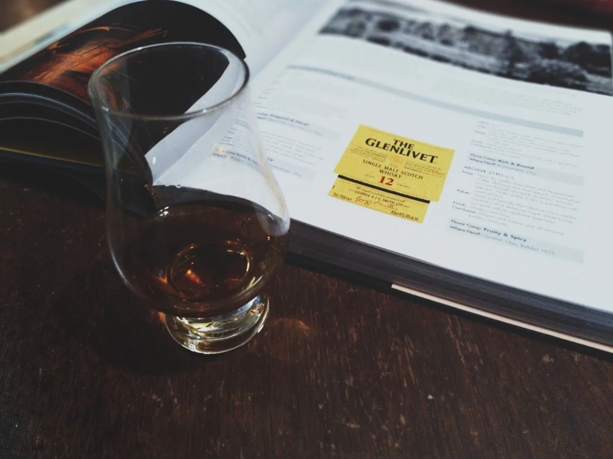 A picture of a dram filled with scotch in front of a book on the history of whisky