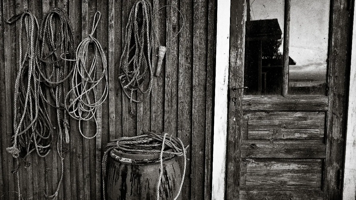 A fisher's hut with ropes and barrels in front. The sunset is reflected in the window of the door.