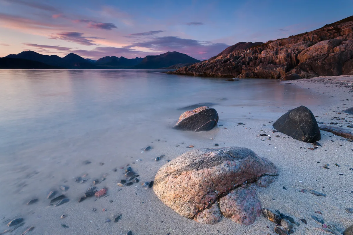 A Bay in Norway at sunset with rocks in the foreground and mountains at the other side of the fjord in the background