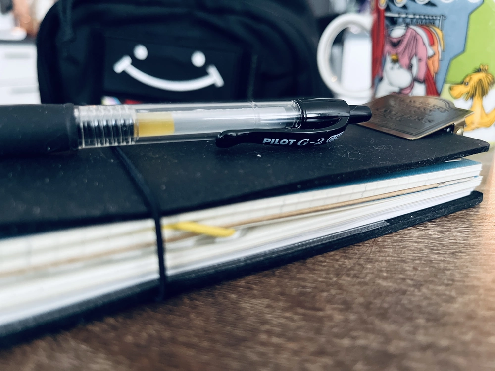 A picture of my black Traverlers Journal with a coffee cup and a Savotta backpack in the background